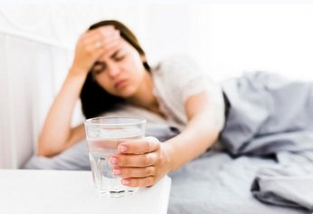 Kranke Frau mit Kopfweh nimmt 1 Glas Wasser: