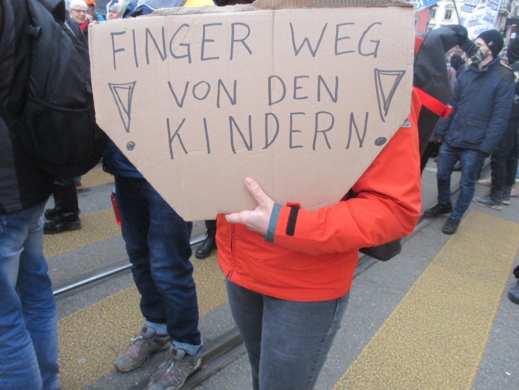Demo in
                  Zurich, Jan.8, 2022 05: Children who have hardly any
                  Corona have not to be vaxxed for sure: "Hands off
                  of our children!" (orig. German: "Finger weg
                  von den Kindern")