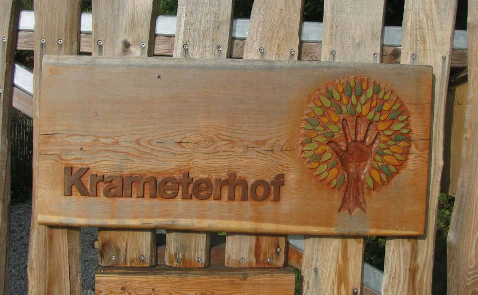 Das Eingangsschild
                              "Krameterhof" aus Holz mit einem
                              Hand-Baum