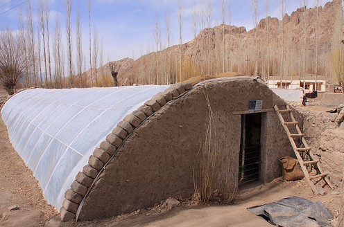La
                            construcción del invernadero medio enterrado
                            en Ladakh, en el norte de la India: Las
                            paredes están enlucidas con arcilla, la lona
                            de plástico está fijada con una hilera de
                            piedras formando el lado de ventanas en
                            forma de una media U.