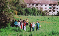 Eine Kindergruppe im Auenpark mit
                          Wohnhaus im Hintergrund