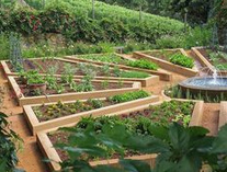 Gartenanlage in Form eines
                          Mandalagartens mit Hochbeeten in Form von
                          Romben und Dreiecken mit Springbrunnen in der
                          Mitte